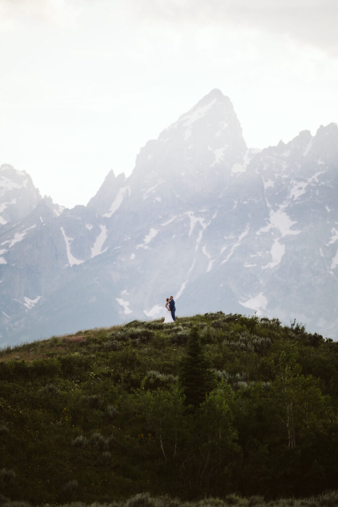 epic couple standing on top of a hill with the Tetons in the background